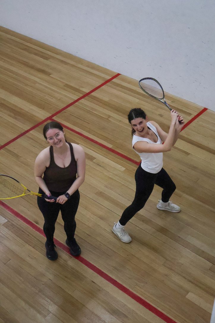Two newbies laughing on court at a squash social