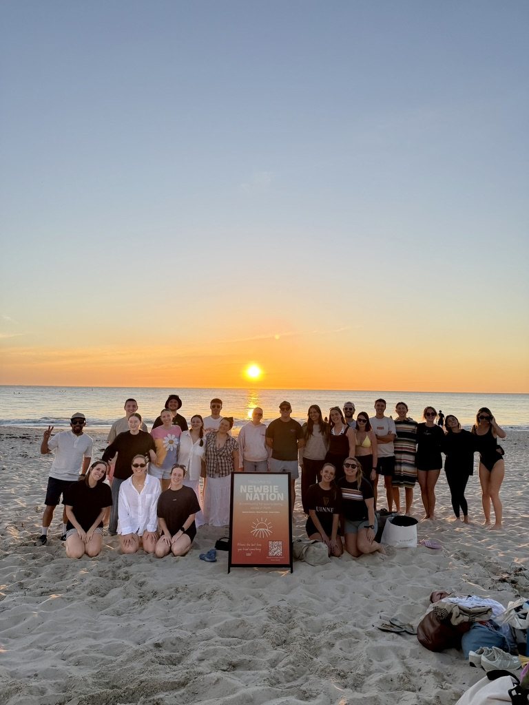Sunset dip group photo on the beach with the Newbie Nation sign