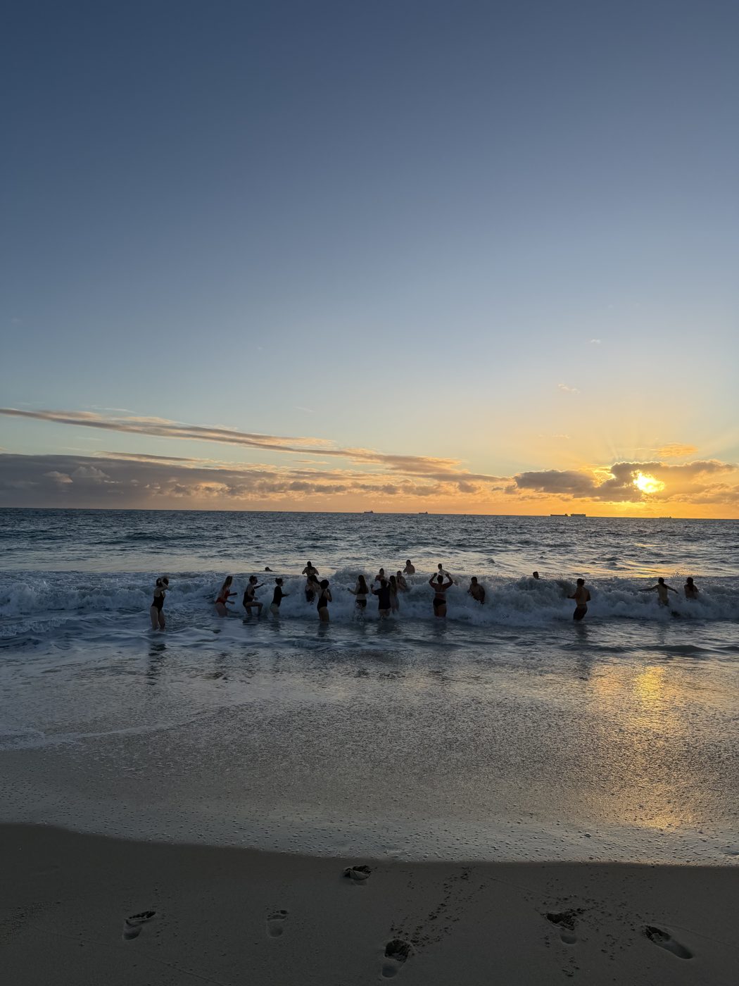 A group wading into the ocean at sunset