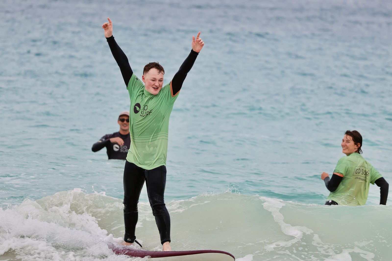 A surfer celebrating with both arms up on a wave
