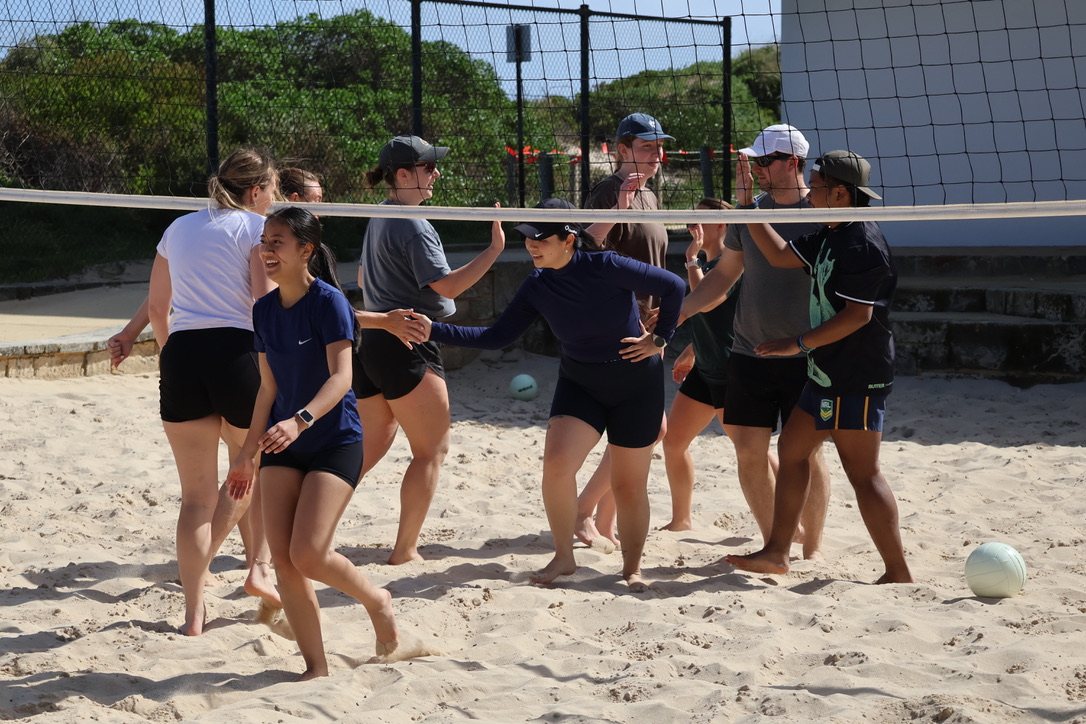 Newbies high-fiving under the net at a beach volleyball social
